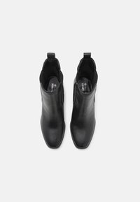 Bottines en cuir noir avec une texture lisse, bout pointu, panneaux latéraux élastiques et tirettes pour un enfilage facile.