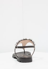 Svart lädersandal med dekorativa silvernitar på remmen, har en texturerad sula och justerbar vristrem.