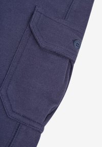 Marinblått tyg med ribbad textur och en ficka med lock som har en knapp, vilket framhäver en skräddarsydd design och detaljerad sömnad.