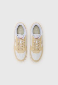 Scarpe da ginnastica beige con dettagli in pelle bianca, punta rotonda e dettagli perforati. Presentano lacci piatti e linguetta con marchio. Suola testurizzata.