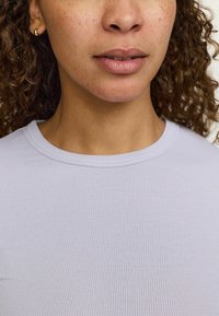 Hellblaue gestreifte T-Shirt mit Rundhalsausschnitt, weichem Textil und sichtbaren Nähten. Auch ein kleiner goldener Creolenohrring ist vorhanden.