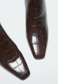 Chaussures en cuir marron avec un motif crocodile brillant et une conception à bout carré sur fond blanc.