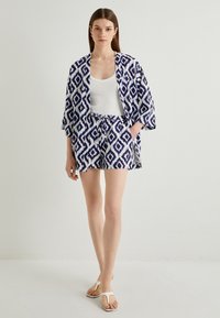 Ensemble kimono et short à motifs bleus et blancs, présentant un design en losanges, en tissu léger et à coupe ample, associé à des tongs blanches.