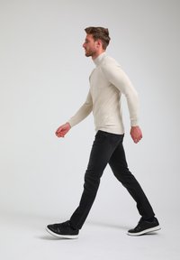 Svetlo bež top z dolgimi rokavi, črne skinny jeans in črne športne copate. Obleka se ponaša z minimalističnim dizajnom in gladko teksturo.