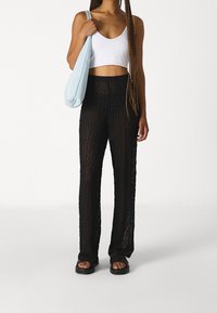 Czarne spodnie z koronkowym wzorem o luźnym kroju, zestawione z białym krótkim topem i jasnoniebieską torebką na ramię. Całość dopełniają czarne klapki.