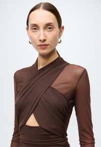 Abito marrone a maniche lunghe con design avvolgente. Caratterizzato da una manica trasparente, dettaglio a taglio e tessuto strutturato che crea un effetto drappeggiato.