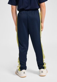 Granatowe spodnie sportowe z limonkowymi paskami po bokach, elastycznym pasem i zwężanym krojem, w połączeniu z białymi i szarymi butami sportowymi.