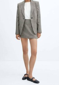 Ensemble de veste et jupe en motif pied-de-poule gris et noir, associé à des chaussures plates noires avec des détails décoratifs.