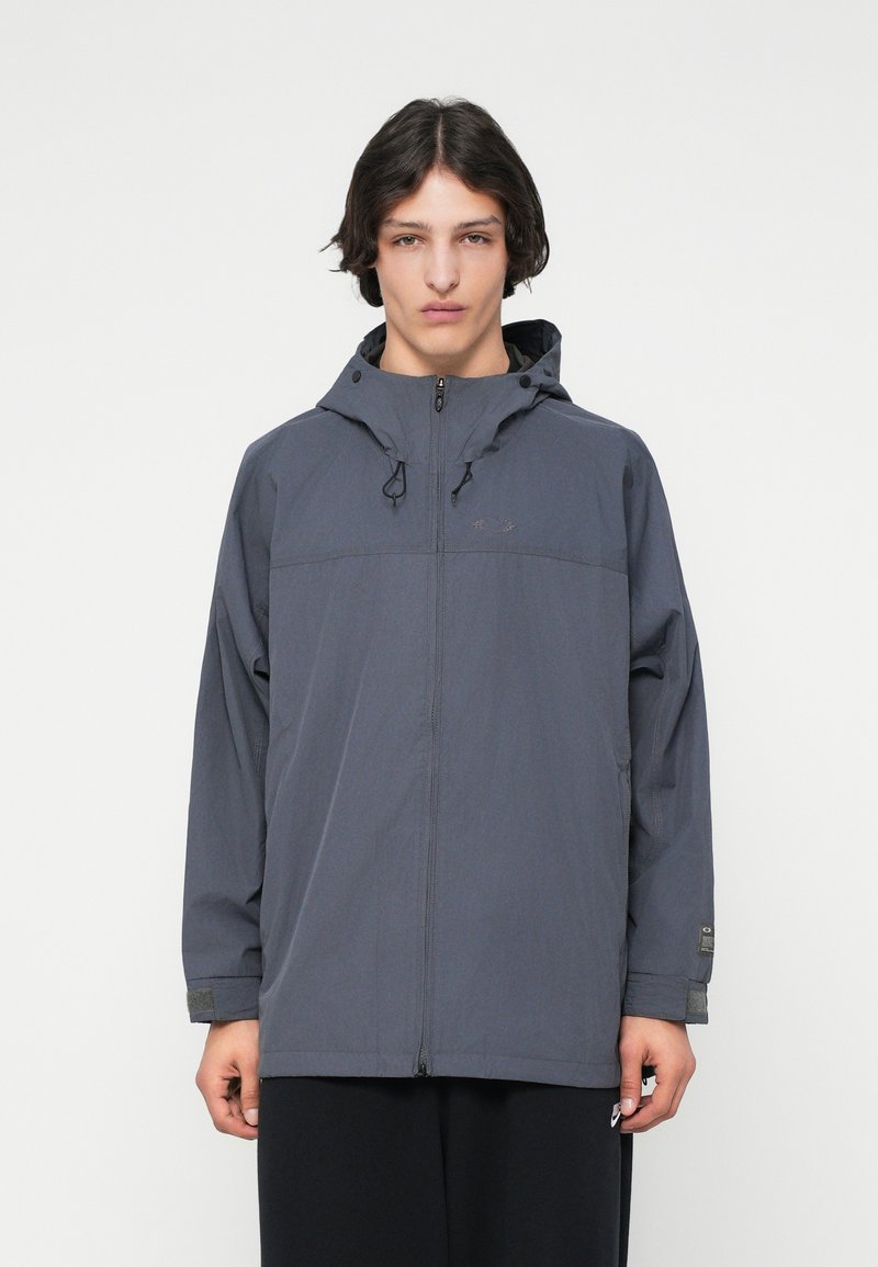 Grijze lichtgewicht jas met verstelbare capuchon, een ritsluiting aan de voorkant en elastische manchetten. Bevat een subtiele logo op de borst en ademende stof.