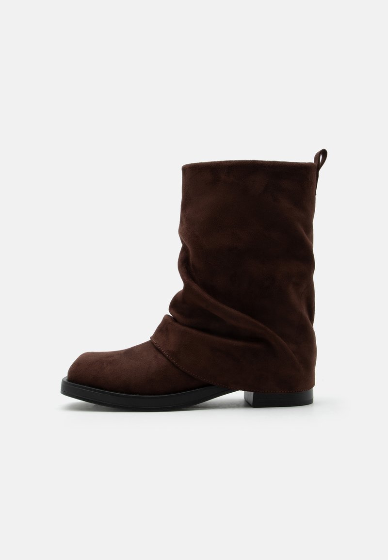 Botte ample mi-mollet en daim marron foncé avec bout rond, petit talon, semelle noire et languette à l'arrière.