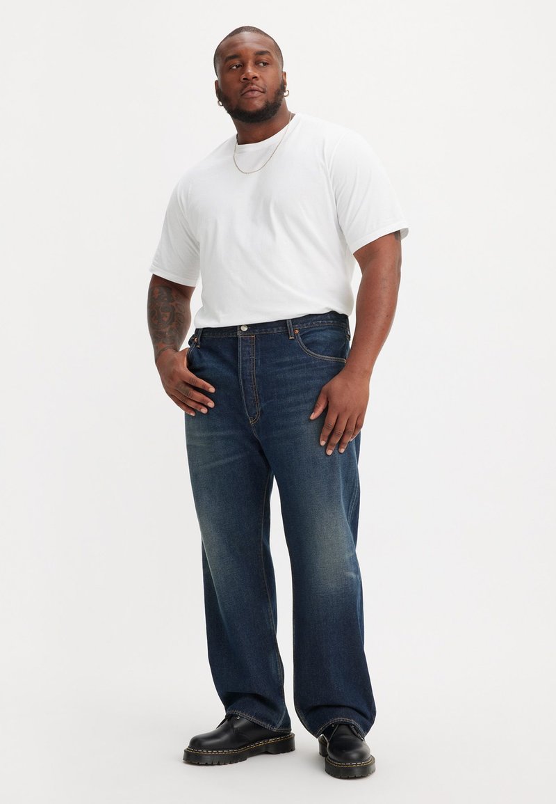 Donkerblauwe spijkerbroek met een rechte pasvorm, gecombineerd met een witte ronde hals t-shirt en zwarte veterschoenen. Minimalistische zichtbare hardware details.
