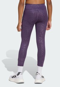 Leggings violettes avec un motif de rayures de tigre texturé, dotés d'une taille haute et d'une coupe fuselée, associés à des chaussures de sport blanches.