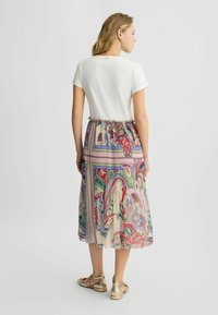 Robe maxi avec un haut blanc et une jupe colorée à motifs avec des designs de paisley dans des teintes de rose, vert et rouge. Sandales dorées.