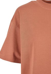 Majica s kratkim rukavima u prigušenoj terracotta boji, izrađena od mekog pamuka, sa zaobljenim izrezom i opuštenim krojem. Glatka tekstura i minimalni detalji.