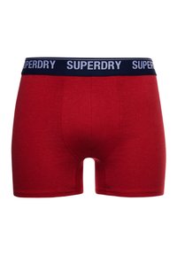 Rode katoenen boxershorts met een marineblauwe tailleband waarop het "SUPERDRY" logo in het wit staat. De stof heeft een gladde textuur en een strakke pasvorm.