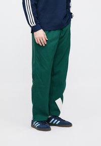 Πράσινο βαμβακερό παντελόνι με φαρδιά εφαρμογή, με λευκή τριγωνική διακόσμηση. Συνδυασμένο με ναυτικά αθλητικά παπούτσια με ανοιχτές γαλάζιες ρίγες.