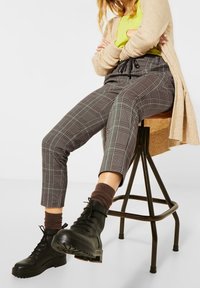 Bottines noires à lacets, pantalon tapered en plaid gris et noir avec une taille à cordon, chaussettes marron et un cardigan beige clair.
