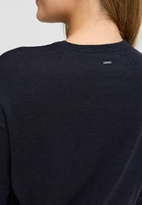 Granatowy sweter robiony na drutach, okrągły dekolt, dopasowany krój, z małą metką z tyłu przy dekolcie. Miękka tekstura, minimalistyczny styl.