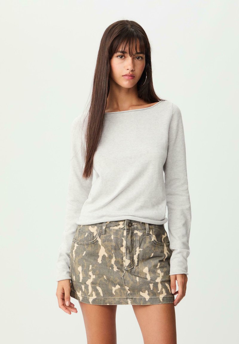 Helles graues Langarmshirt mit einem Bootsausschnitt, kombiniert mit einem Jeansrock im Camouflage-Muster in Grüntönen und Beige; lässige Passform und strukturierter Stoff.