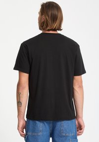 Camiseta de algodón negra con mangas cortas y cuello redondo. Diseño sencillo, textura suave y dobladillo recto en la parte inferior.
