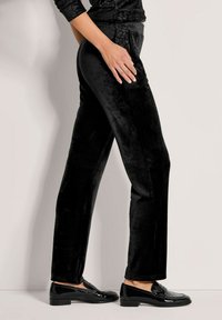 Zwarte fluwelen broek met een rechte pasvorm en een elastische tailleband, met een gladde textuur en gecombineerd met glanzende zwarte loafers.
