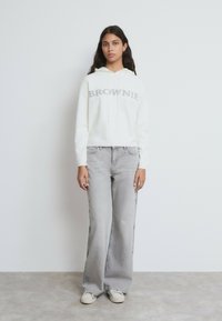 Sudadera blanca con la palabra "BROWNIE" escrita en gris, combinada con jeans de pierna ancha en gris claro con bordados de estrellas, y zapatillas blancas.