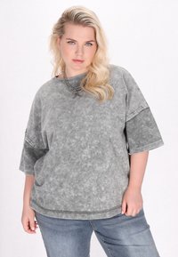 Grå oversized t-shirt i en udvasket stil med en tekstureret overflade og kontrasterende mørke ærmer. Kombineret med blå jeans.