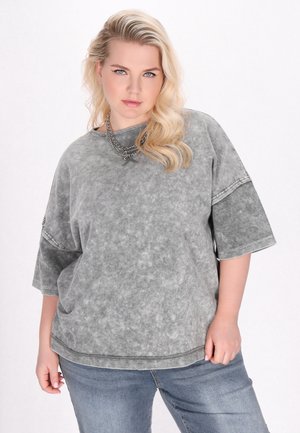 Grå oversized t-shirt i en udvasket stil med en tekstureret overflade og kontrasterende mørke ærmer. Kombineret med blå jeans.