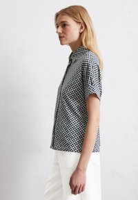 Kurzarmhemd mit einem geometrischen Schwarz-Weiß-Muster, ausgestattet mit einem Button-Down-Kragen und leichtem Stoff für eine gute Atmungsaktivität.