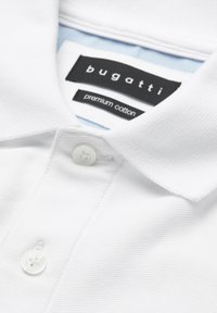Weißes Baumwollpolohemd mit Kragen, zwei Knöpfen und schwarzen Etiketten mit der Aufschrift "Bugatti" und "Premium Cotton" im Nacken.