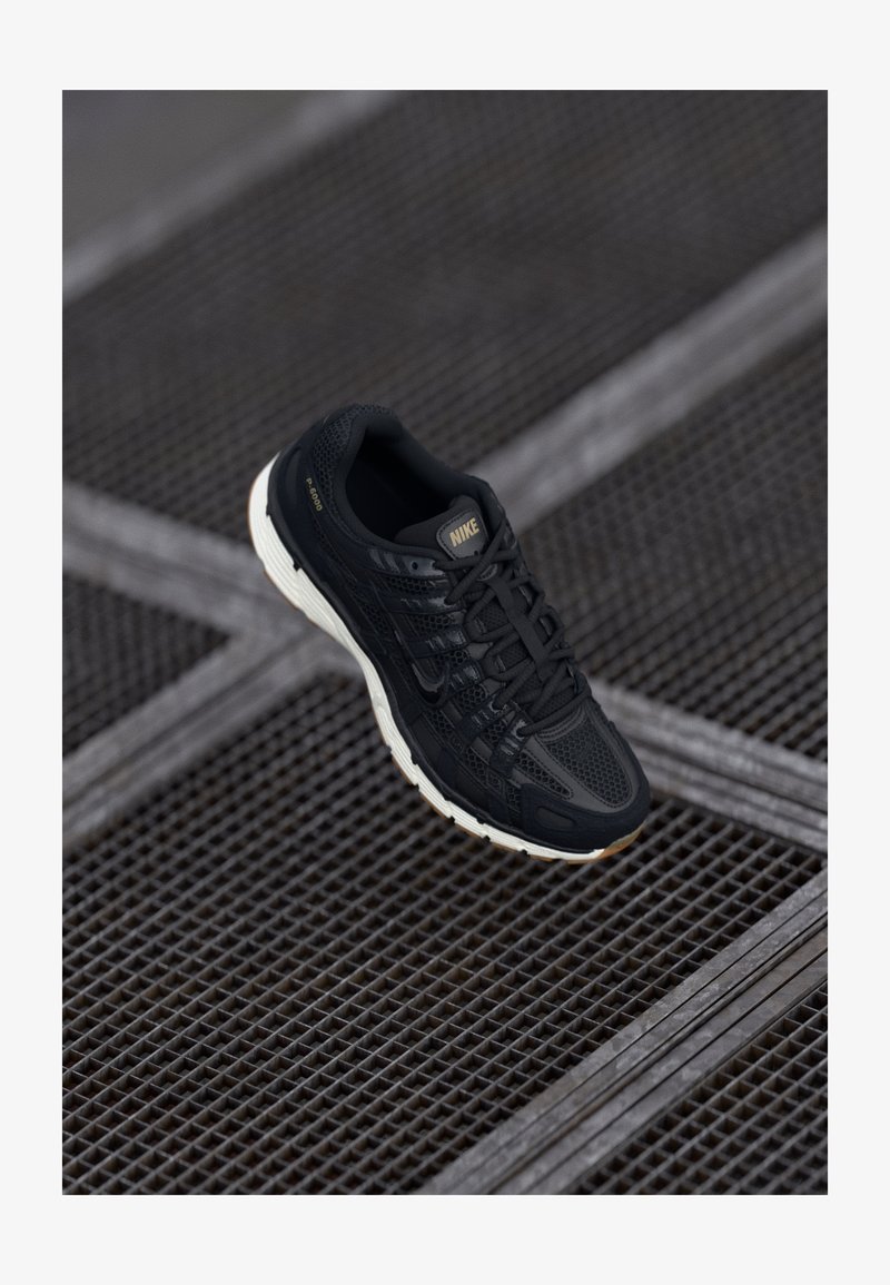 Crna Nike trkačka cipela s teksturiranim mrežastim gornjim dijelom, gumiranim potplatom i suptilnim zlatnim akcentima. Ima dizajn s vezicama i udoban potplat.