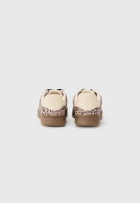 Sneakers with a light beige upper featuring a leopard print pattern, complemented by a brown rubber sole and contrasting black accents.