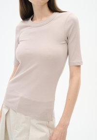 Vaalea taupe ribattu paita, jossa on pyöreä pääntie ja lyhyet hihat. Ominaisuuksiin kuuluu slim fit -malli ja hillitty logo helmaosassa. Pehmeä kangas.