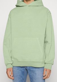 Sudadera con capucha color verde menta hecha de tela suave que presenta un bolsillo tipo canguro, mangas largas y una capucha grande. Textura lisa con puños acanalados.
