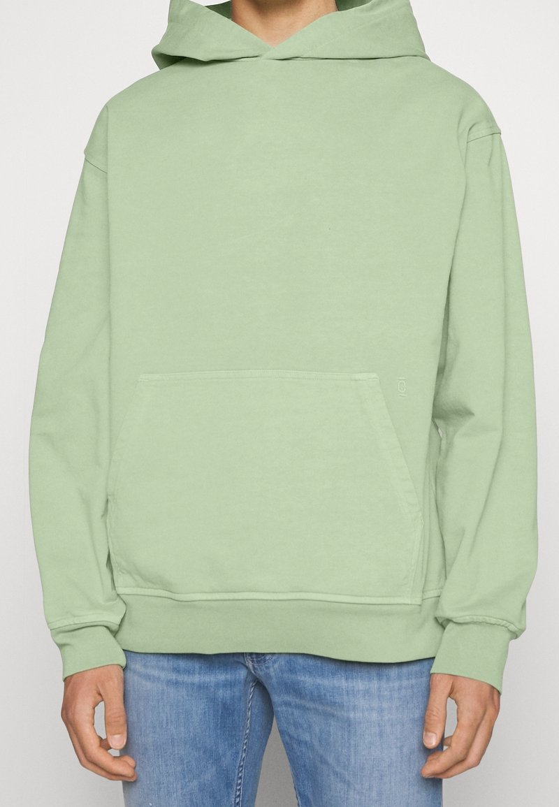 Sudadera con capucha color verde menta hecha de tela suave que presenta un bolsillo tipo canguro, mangas largas y una capucha grande. Textura lisa con puños acanalados.