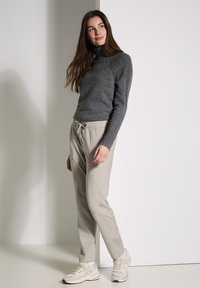 Grå polotröja och beige byxor med elastisk midja och fickor, kompletterat med ljusgrå sneakers med en texturerad design.