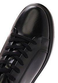Black leather sneaker with a shiny finish, featuring black laces, a rounded toe, and a smooth texture. Minimalistic design and no visible logos.