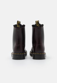 Botas de tornozelo de couro bordô com solas texturizadas pretas, detalhes em costura amarela e forro de pelo, apresentando alças para facilitar o calçar.