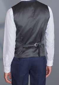 Grau satinierter Weste mit einer glatten Textur, einem Rückengurt und einer Schnalle, getragen über einem weißen Hemd und kombiniert mit dunkel karierten Hosen.