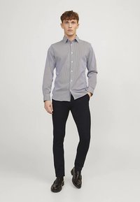 Overhemd met verticale donkerblauwe en witte strepen, lange mouwen, kraag, gecombineerd met donkere broek en zwarte schoenen. Gladde stoftextuur.