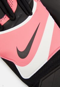 Guanto Nike nero e rosa con finitura liscia, caratterizzato da uno swoosh bianco e accenti neri testurizzati. Le cuciture dettagliate sono visibili.