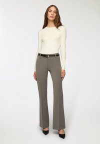 Jasno beżowa bluzka z długim rękawem w połączeniu z szarymi spodniami o kroju prostym, które mają czarny pasek z akcentami ze złotego metalu.