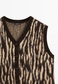 Gilet en maille sans manches avec motif rayé abstrait noir et beige et boutons noirs, doté d'un col en V et d'une texture duveteuse.