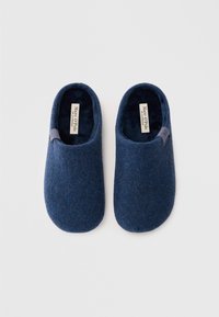 Pantofole in feltro blu navy con una superficie morbida e testurizzata, forma arrotondata e un dettaglio elastico per facilitare l'indossamento. Etichetta del marchio visibile all'interno.