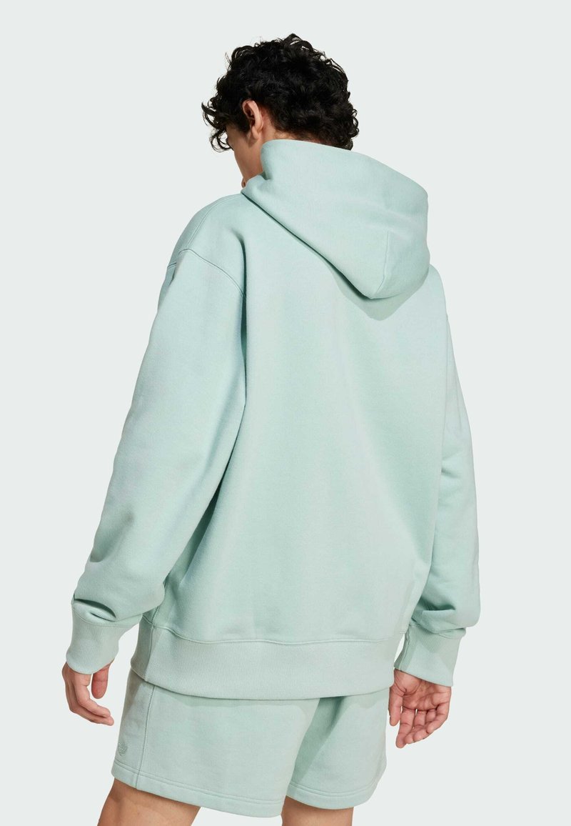 Jasno miętowy hoodie wykonany z miękkiego materiału, z dużym kapturem, opadającymi ramionami i prążkowanymi mankietami. Krój jest luźny.