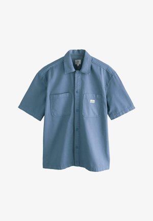 Rövid ujjas, gombos ing világoskék pamut anyagból, két elülső zsebbel és klasszikus gallér kialakítással.