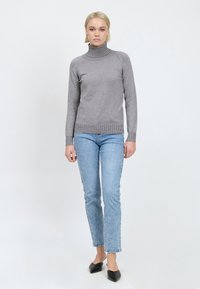 Maglione grigio a collo alto con dettagli a coste, abbinato a jeans diritto azzurri e ballerine nere a punta, su sfondo bianco.