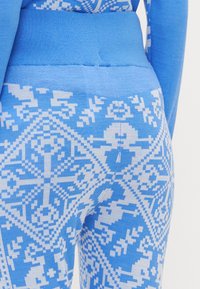 Blå mønstrede leggings med et teksturert design som har hvite geometriske former. Mykt stoff med en bred blå midjebånd.
