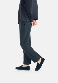 Marineblå ruskinds loafers med en struktureret finish, med slip-on design og diskrete syninger, båret med løst siddende mørke bukser.