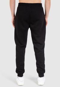 Schwarze Jogginghose mit elastischem Bund und Säumen, aus einem glatt strukturierten Stoff. Die Passform ist an den Knöcheln schmaler.